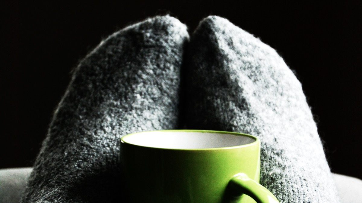 Fluffy grey socks on feet with a green mug in front of them