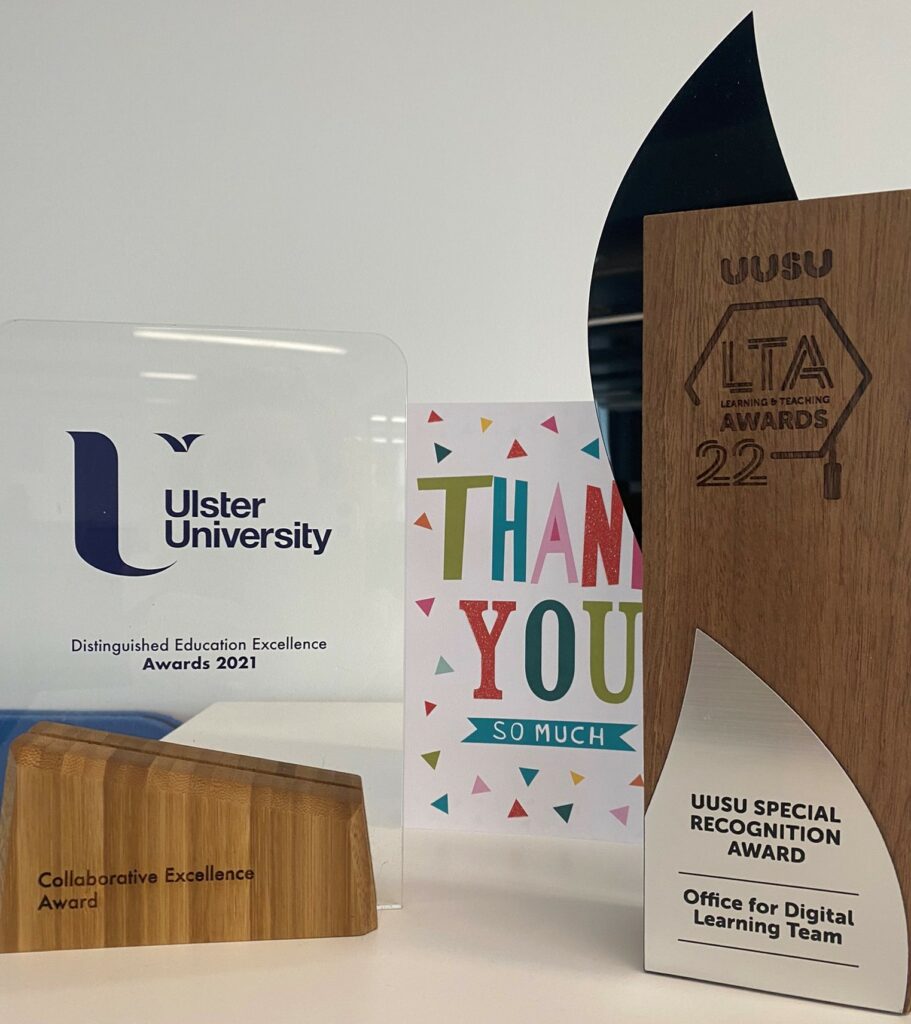 Two award trophies, one made of glass and wood stand and the other a wooden stand with silver plaque and thank you card in the middle. 