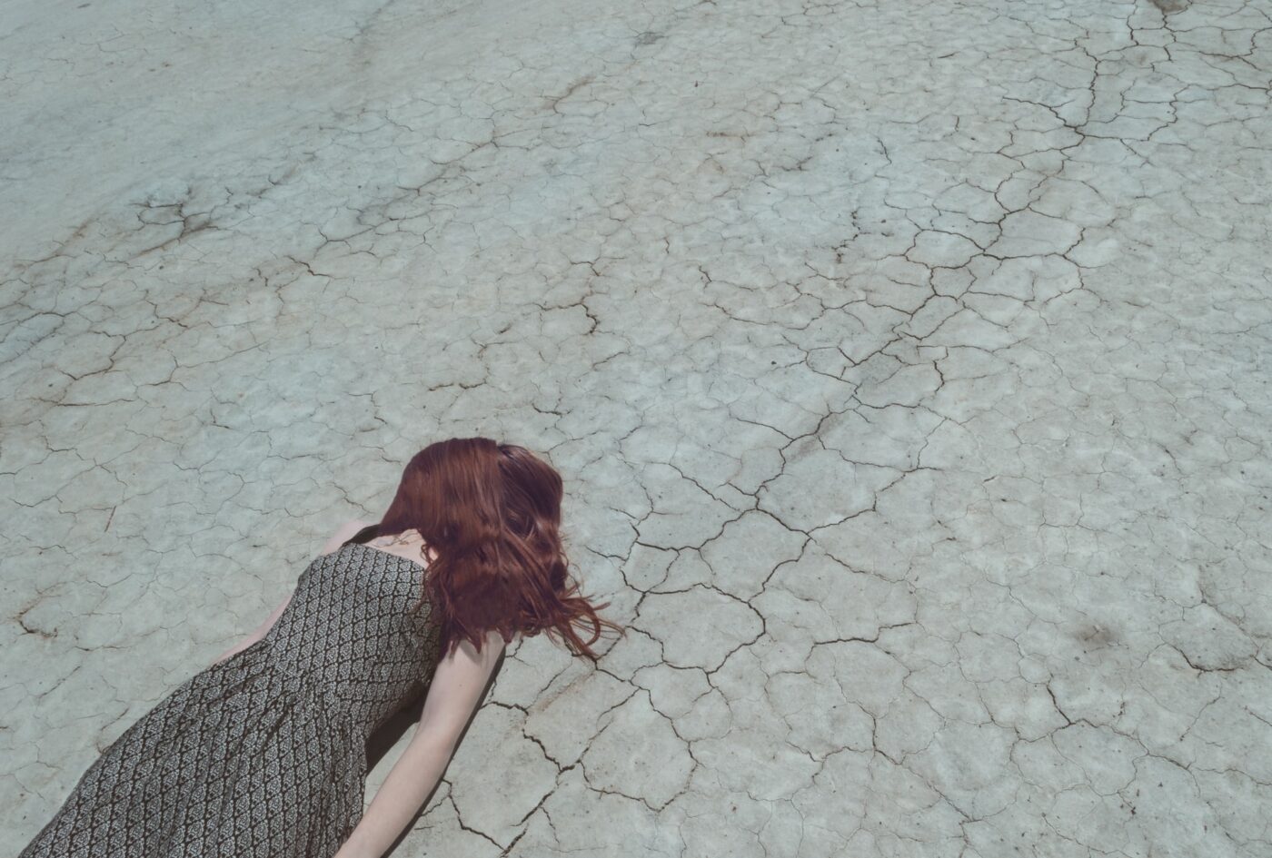 woman lying facedown on dry cracked outdoor surface