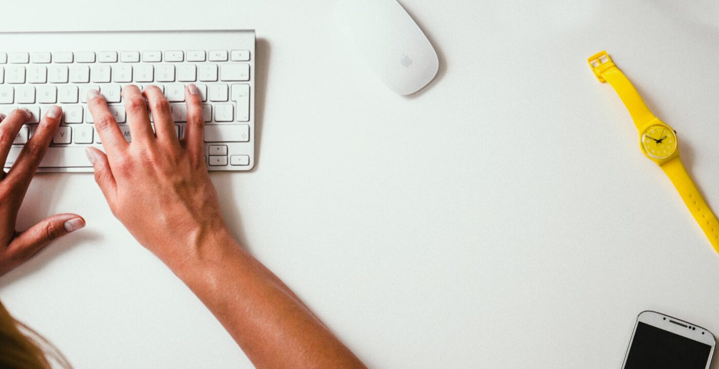 Desk with keyboard, watch, mouse and hands typing