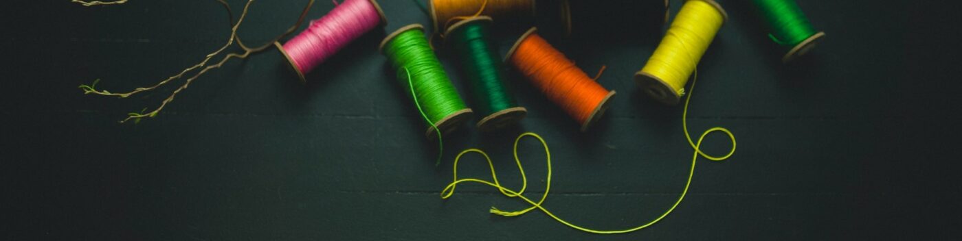 spools of bright colours on a dark plain surface with one thread pulled from one across the surface.